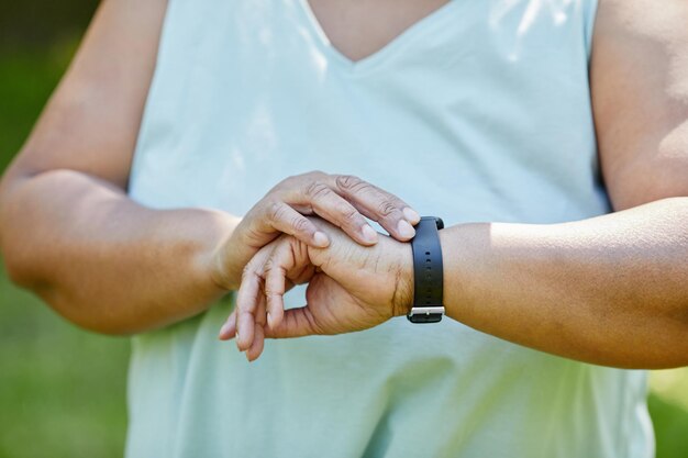 Gros plan sur une femme noire en surpoids installant une montre de fitness pendant l'entraînement en plein air dans le parc