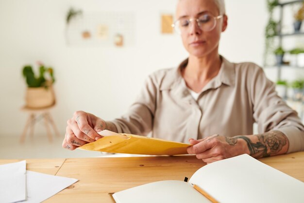 Gros plan d'une femme occupée avec des tatouages assis à table et emballant des documents dans une enveloppe au bureau