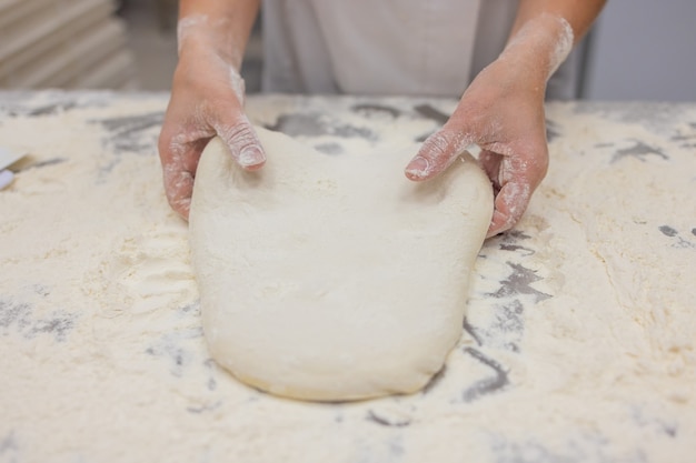 Gros plan de femme pétrir la pâte à pizza.