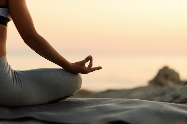 Gros plan sur une femme pratiquant le yoga en position du lotus au coucher du soleil. Copiez l'espace.