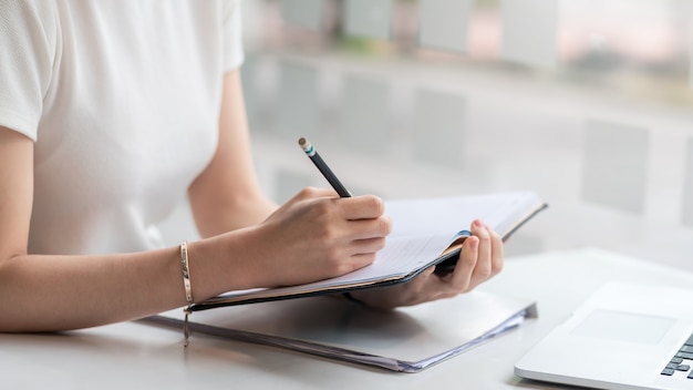 Gros plan d'une femme prenant des notes avec un ordinateur portable à la maison.