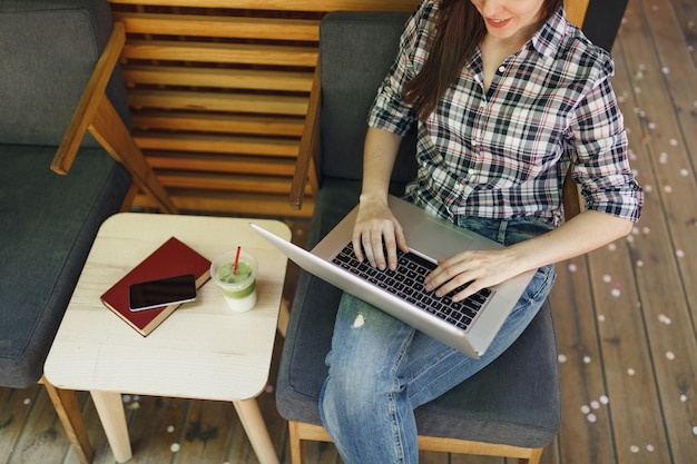 Gros plan sur une femme recadrée dans un café de rue en plein air, un café en bois assis dans des vêtements décontractés, travaillant sur un ordinateur portable moderne pendant le temps libre. Bureau mobile