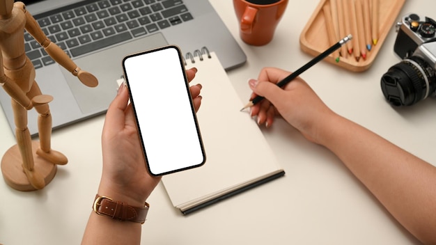 Gros plan Femme recherchant des articles sur un smartphone et prenant des notes sur un bloc-notes en spirale