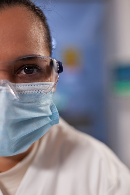 Photo gros plan d'une femme scientifique avec des lunettes et un masque facial dans un laboratoire médical à la clinique. docteur professionnel en analyse avec équipement de sécurité et appareils de microbiologie pour la recherche