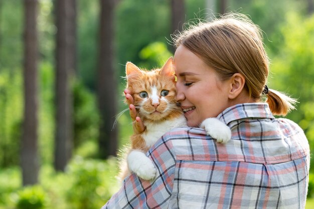 Gros plan d'une femme souriante en chemise à carreaux étreignant et embrassant avec tendresse et amour chat triste excité domestique à l'extérieur.