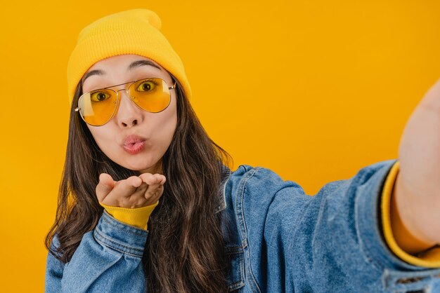 Gros plan d'une femme souriante faisant une photo de selfie sur un smartphone isolé sur fond jaune