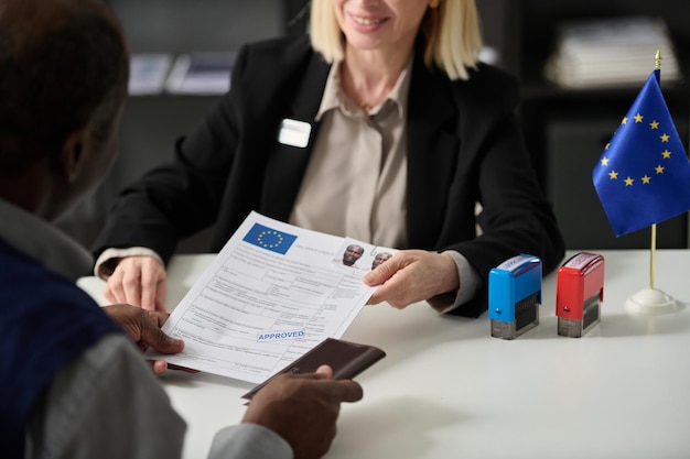 Gros plan sur une femme souriante remettant un formulaire de demande de visa approuvé à un homme noir au bureau de l'immigration