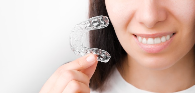 Gros plan femme tenant un accolades amovibles transparentes pour un sourire parfait. Aligneurs orthodontiques pour