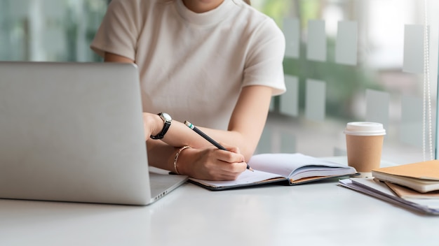 Gros plan d'une femme tenant un crayon et prenant des notes au bureau.