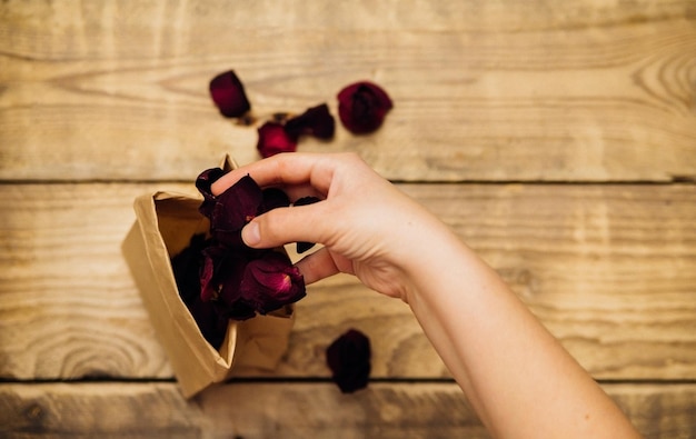 Gros plan d'une femme tenant un sac en papier brun avec des pétales de rose séchés à la main.