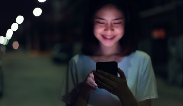 Gros plan de femme tenant un smartphone pendant la nuit dans la rue Technologie pour le concept de communication.