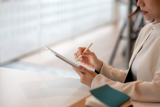Gros plan d'une femme tenant un stylo avec une tablette au bureau.