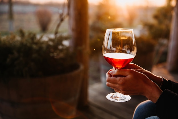 Gros plan d'une femme tenant un verre de vin rouge dans la lumière du coucher du soleil sur une terrasse