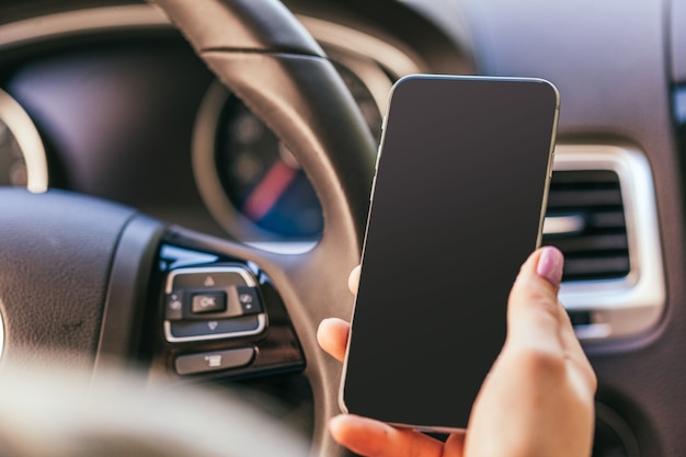 Gros plan d'une femme utilisant un smartphone en conduisant une voiture