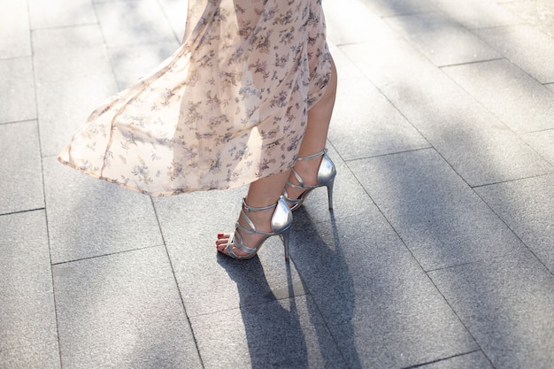 Gros plan d'une femme vêtue d'une robe et de chaussures à talons argentées marchant le long d'une rue urbaine pavée. journée mondiale du tourisme