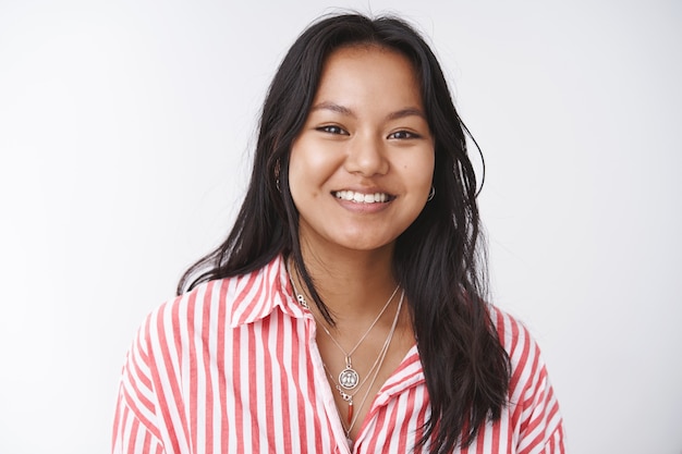 Gros plan d'une femme vietnamienne attrayante et optimiste en blouse rayée riant et souriant exprimant joyeusement une humeur positive et un sens de l'humour posant sur fond blanc