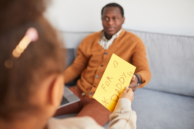 Gros plan d'une fille afro-américaine méconnaissable offrant un cadeau surprise à papa le jour de la fête des pères, espace de copie