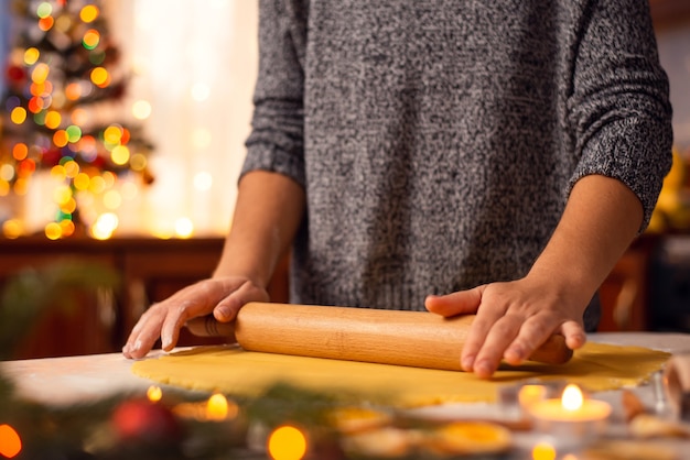 Gros plan d'une fille aplatissant la pâte à l'aide d'un rouleau à pâtisserie préparant de délicieux biscuits de Noël