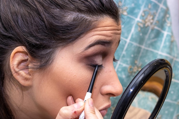 Gros plan d'une fille appliquant un eye-liner tenant un miroir Jolie fille appliquant un eye-liner tenant un miroir