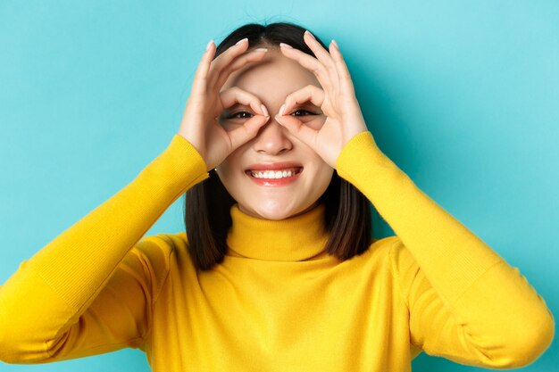 Gros plan d'une fille asiatique drôle regardant à travers des lunettes à main et souriant