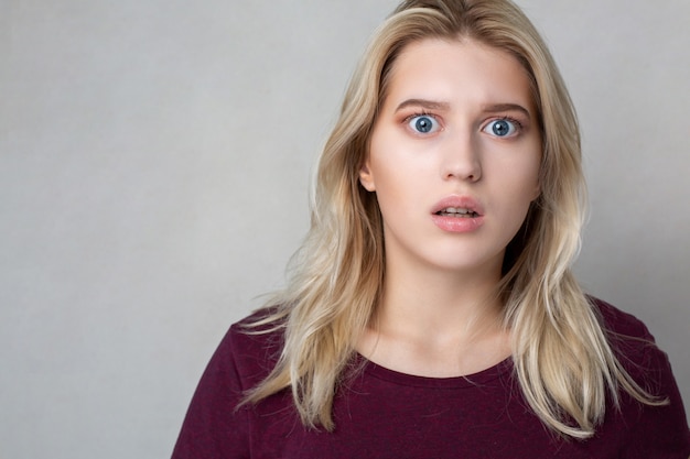 Gros plan d'une fille blonde choquée debout sur un mur gris. Espace pour le texte