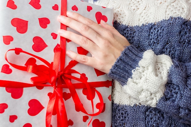 Gros plan d'une fille européenne dans un pull tricoté tenant une boîte-cadeau rouge dans ses mains. Concept commercial, cadeaux de nouvel an et de Noël