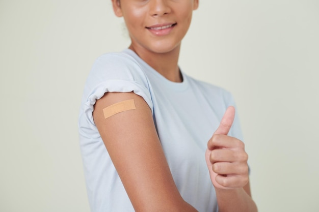 Gros plan d'une fille montrant le pouce vers la caméra et souriant, elle se fait vacciner contre le coronavirus