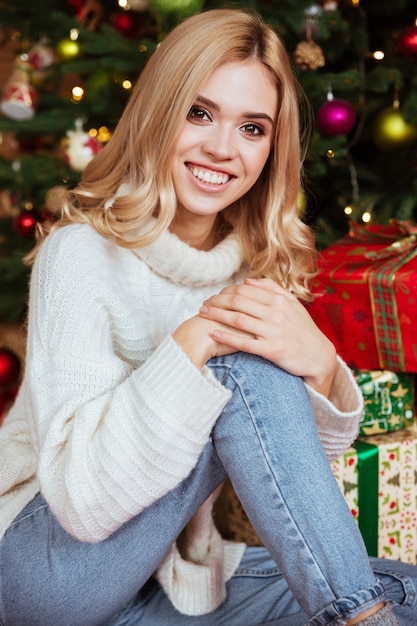 Gros plan fille en pull assis sur le sol près du sapin et des cadeaux.