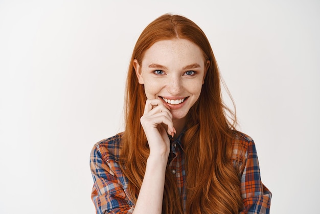 Gros plan d'une fille rousse stupide regardant la caméra en souriant avec des dents blanches et un visage heureux debout sur fond blanc Espace de copie