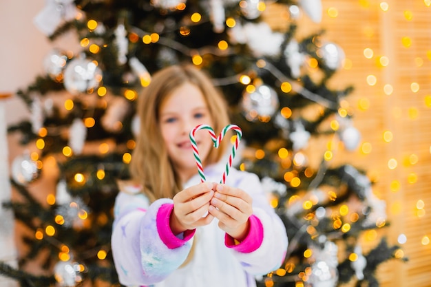 Gros plan d'une fille tenant des bonbons en forme de coeur avec un arbre de Noël scintillant derrière. faible profondeur de champ en mettant l'accent sur les mains.