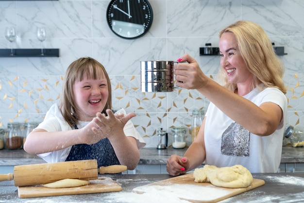 Gros plan d'une fille trisomique et de sa charmante mère qui prépare des tartes à la pâte