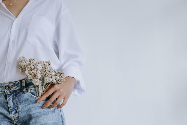 Gros plan d'une fleur d'haleine de bébé séchée sur une poche de jean tenue par une jeune fille élégante dans un style décontracté