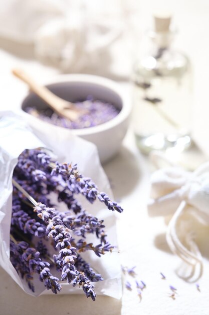 Gros plan sur des fleurs de lavande sèches dans du papier calque blanc Sachets de lavande faits à la main sur une nappe en coton Décorations rustiques à faible impact Cuillère en bois dans un bol avec des fleurs de lavande sèches