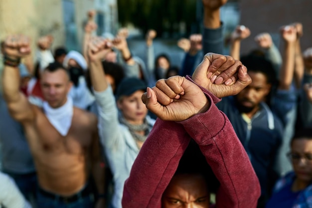 Gros plan sur une foule de personnes aux poings serrés au-dessus de la tête protestant dans les rues