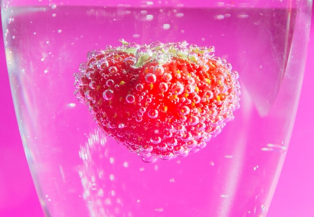 Gros plan, fraise dans l'eau avec des bulles sur fond rose.