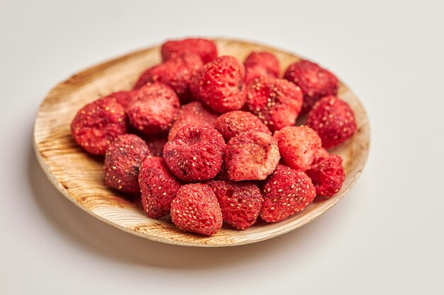 Gros plan de fraises déshydratées dans un bol en bois isolé sur blanc.