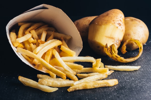 Gros plan de frites avec des pommes de terre crues sur fond noir.