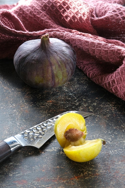 Gros plan sur les fruits d'automne poire jaune figue violette et prunes jaunes avec un couteau de cuisine fond brun texturé foncé et torchon de cuisine bordeaux magenta