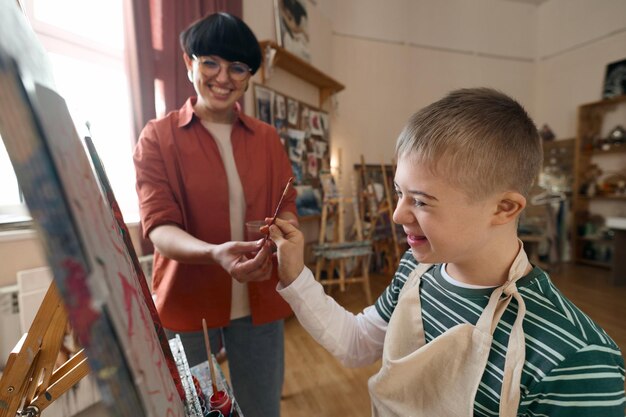 Photo en gros plan, un garçon heureux avec un handicap tenant un pinceau et appréciant le cours d'art