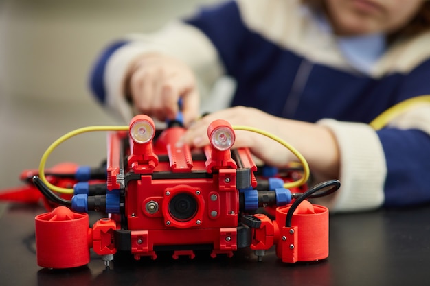 Gros plan sur un garçon méconnaissable construisant une machine robotique rouge tout en profitant d'un cours d'ingénierie à l'école de développement, espace de copie