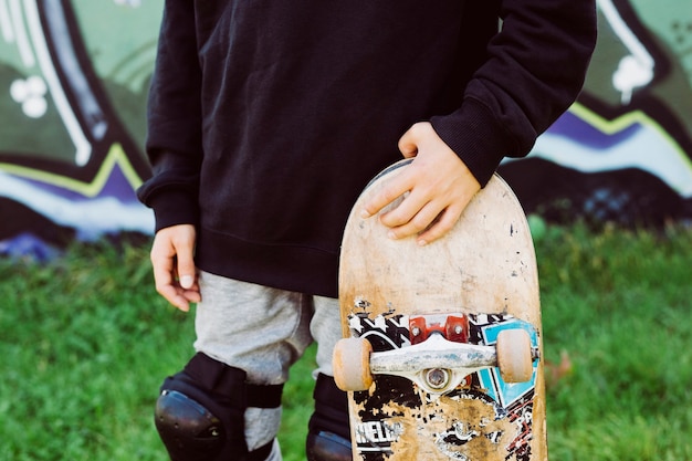 Gros plan d'un garçon patineur avec une vieille planche à roulettes en face d'une fresque graffiti