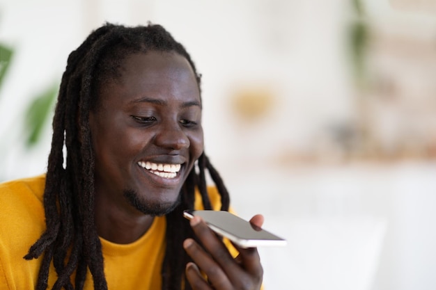 Gros plan d'un gars noir heureux à l'aide d'un smartphone pour enregistrer un message vocal