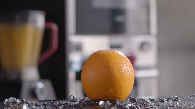 Gros plan de la glace tombant sur l'orange, mixeur avec du jus au premier plan. Boissons à l'orange fraîches et saines