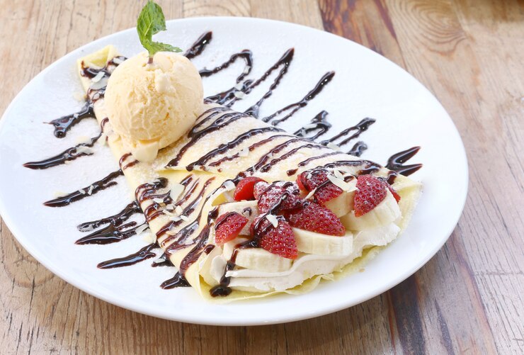 Gros plan de glace à la vanille avec des crêpes et des fraises sur un bureau en bois