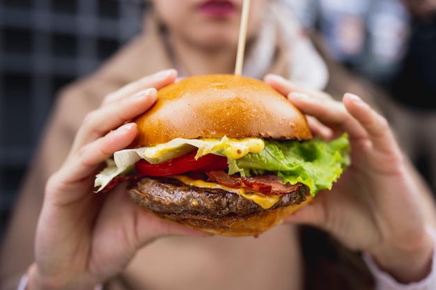 Gros plan gourmet savoureux burger au bacon. Chignon femelle méconnaissable.