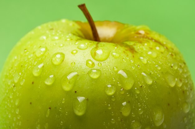 Gros plan sur des gouttes d'eau sur une pomme verte fraîche sur fond vert, faible profondeur de champ.