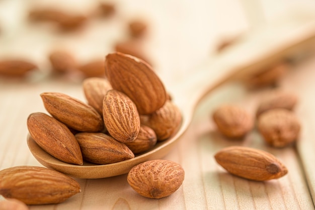 Gros plan de graines d'amandes fraîches brunes dans une cuillère en bois sur table en bois.