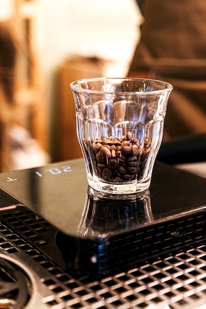 Gros plan des grains de café à l'intérieur du verre à shot sur l'échelle de poids numérique.