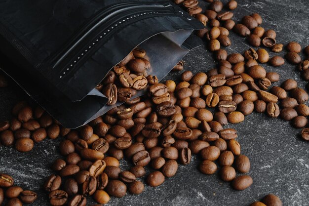 Gros plan sur des grains de café torréfiés renversés par des emballages de café noir