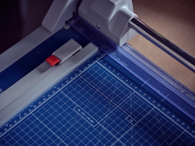 Gros plan en grand angle d'une machine de découpe professionnelle moderne avec du papier millimétré bleu placé sur une table dans un atelier de reliure